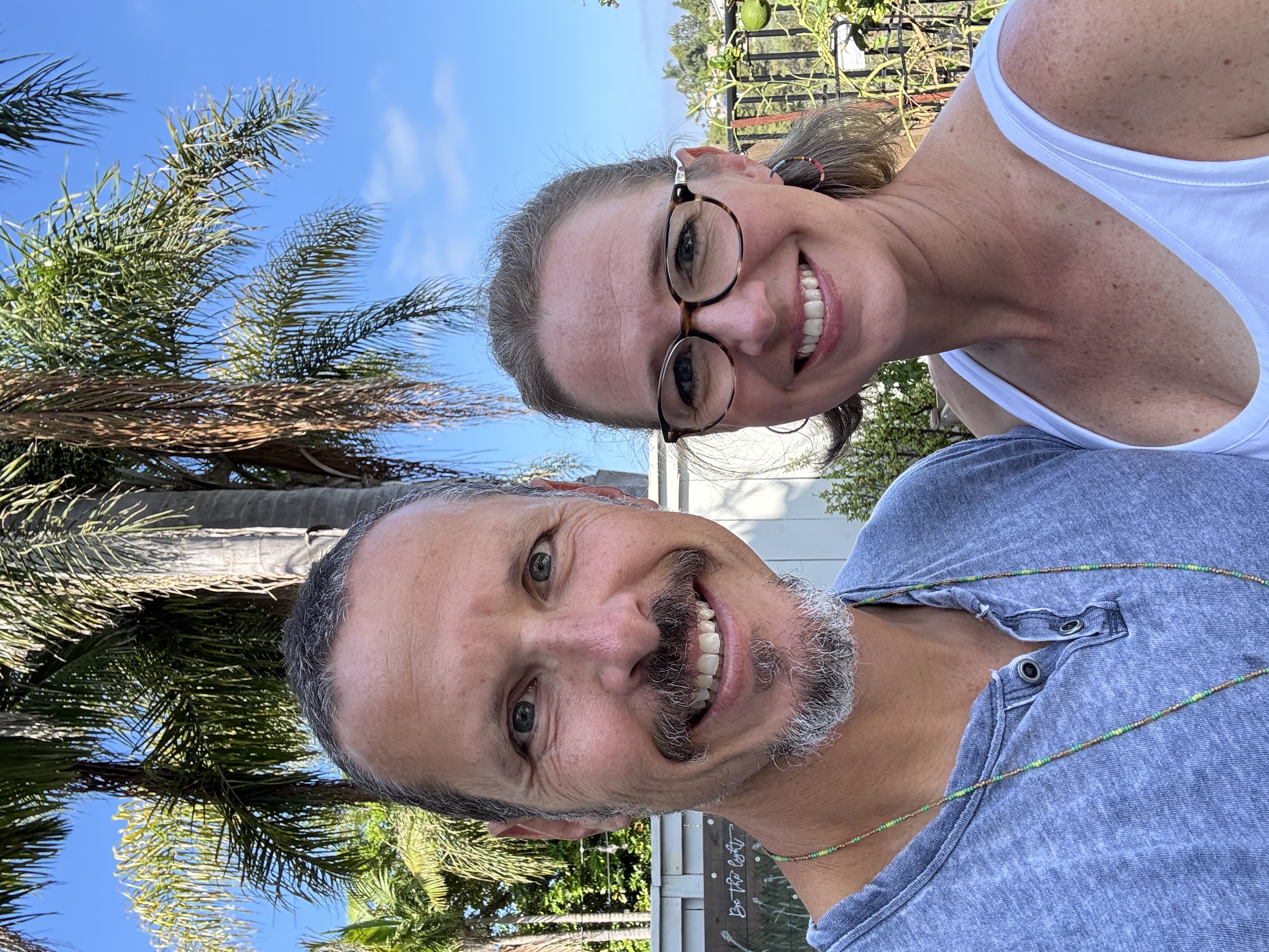 Jason Newmark and his wife Shelese smiling together outdoors beneath palm trees